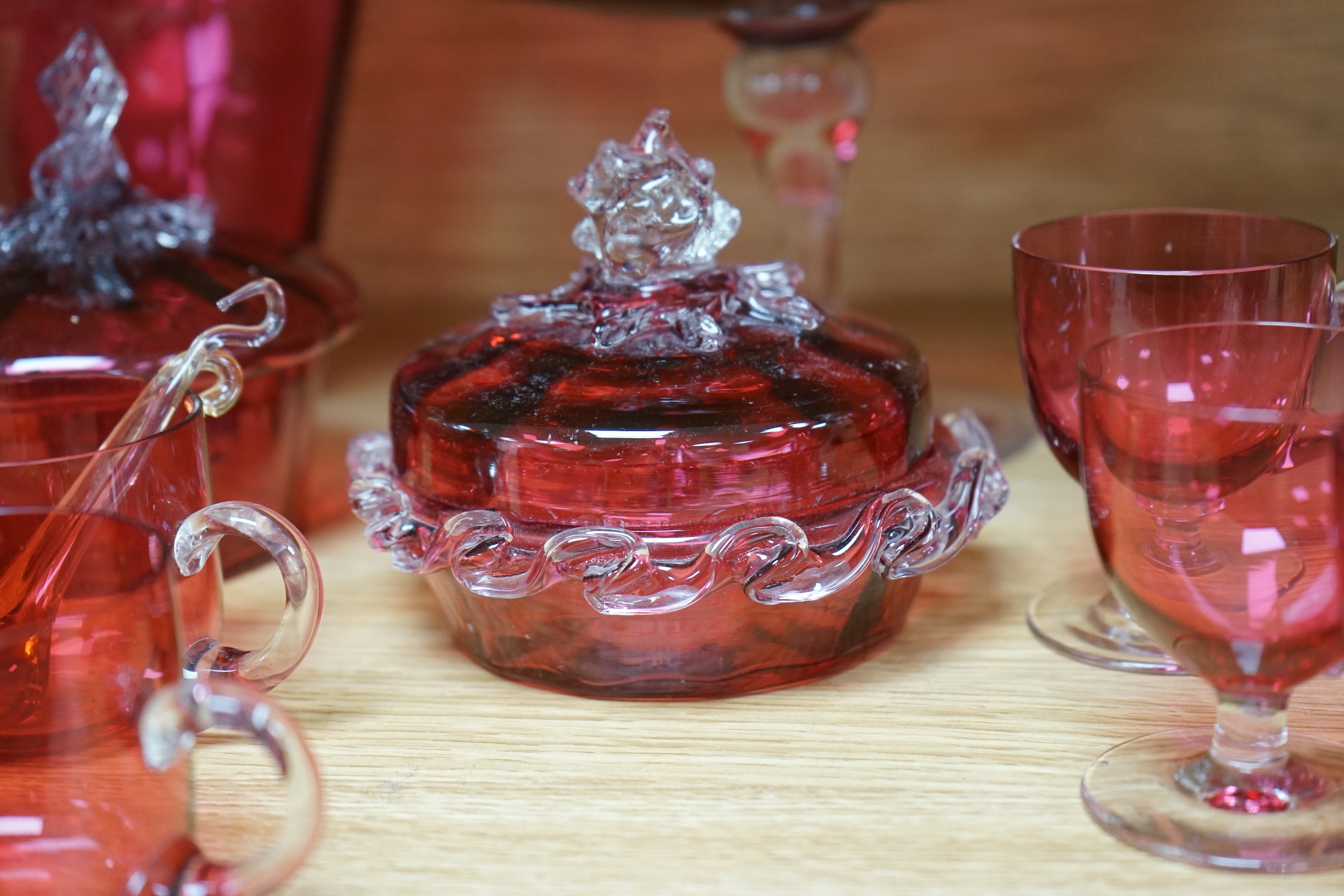 Mixed cranberry glassware to include jugs, glasses, jars and a comport, largest 23cm high. Condition - fair to good